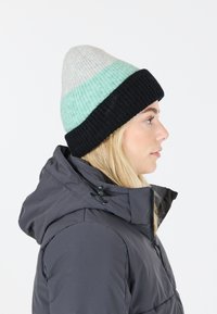 Stickad mössa med tre färgsektioner: ljusgrå längst upp, mintgrön i mitten och svart ribbad accent i basen.