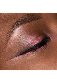 Nærbillede af et øjenlåg med en skinnende pink øjenskygge og en mørk eyeliner på en mørk hudtone, hvor den teksturerede hud er synlig.