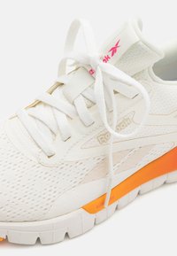 Scarpa sportiva Reebok in bianco e rosa chiaro, con tomaia in rete traspirante, lacci piatti e un vivido accento arancione sulla suola.