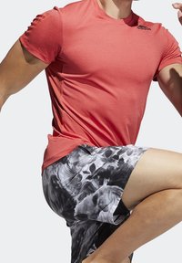 Rød atletisk T-shirt med et struktureret mønster, kombineret med sort-hvide tie-dye shorts. Begge beklædningsgenstande har en tætsiddende pasform og korte ærmer.