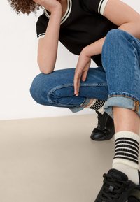 Černé žebrované tričko s bílým lemováním, světle modré krátké džíny, černé tenisky a pruhované ponožky. Na neutrálním pozadí.