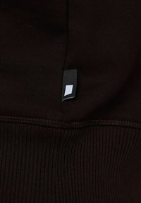 Tessuto nero con una finitura a coste testurizzate. È visibile un piccolo etichetta nera con un design geometrico bianco.