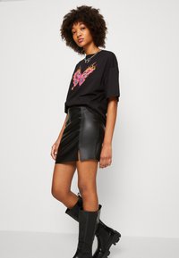 T-shirt grafico nero con un vivace design di farfalla, abbinato a una mini gonna in pelle nera con uno spacco frontale e stivali neri al ginocchio.