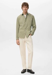 Camisa de manga larga de color verde claro combinada con pantalones color crema y zapatos negros. Corte ajustado, tela suave y diseño de cuello clásico.