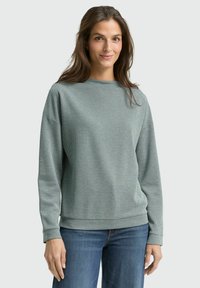 Light green patterned sweatshirt with long sleeves, round neckline, and ribbed cuffs; worn with blue jeans. Soft texture and relaxed fit.