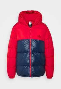 Röd och marinblå pufferjacka med huva, dragkedjestängning, elastiska ärmmuddar och en broderad logotyp på bröstet. Glansig textur med kviltade sektioner.