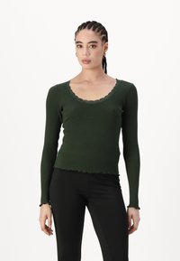 Grønn ribbet langermet topp med skåret nakke og kant. Materialet har en myk tekstur. Pyntet med blonder detaljer ved nakken.