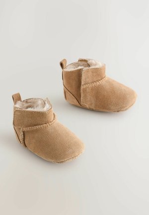 Bottes en suede beige avec une douce doublure en fourrure, au design bas, et un accent cousu autour de la cheville, dotées d'une languette à l'arrière.