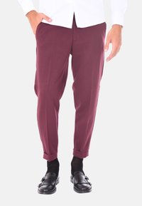 Pantaloni tailored bordeaux con una texture liscia, dotati di orlo con risvolto e tasche laterali, abbinati a mocassini neri e calzini scuri.