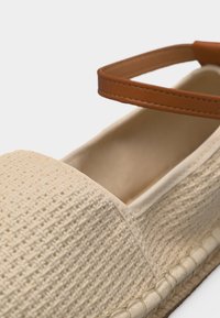 Μπεζ πλεκτό παπούτσι εσπαντρίγια με δερμάτινο ταμπά λουράκι αστραγάλου και μαξιλαράκι στο πέλμα, κοντινή όψη στη μύτη και το λουράκι.