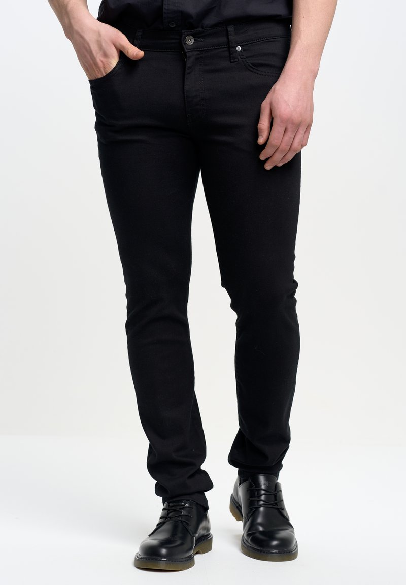 Jeans negros ajustados de mezclilla con una textura suave. Presentan bolsillos frontales, un cierre de botón y un diseño de pierna recta. Llevados con zapatos negros.