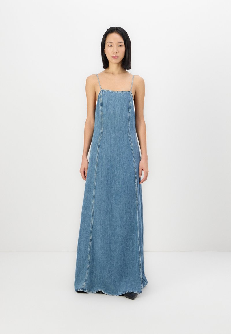 Denim maxikjole i lys blå, med tynne skulderstropper, en tettsittende liv, og en utsvingt kant med synlige sømdetaljer.