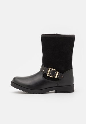 Botte noire mi-mollet avec pied en cuir lisse, dessus en daim, bride décorative à boucle dorée et talon bas à bloc sur fond blanc.