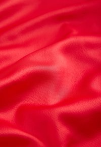 Červená saténová látka, hladká textura, jemně se skládá do záhybů, odráží světlo, s jemným leskem, bez viditelných vzorů nebo kovových částí.
