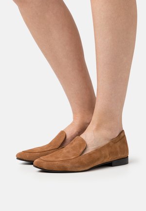 Mocassins en daim marron avec un talon plat, dotés d'une pointe arrondie et d'un design à enfiler. Texture lisse avec peu de détails de couture.