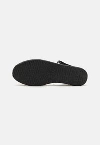 Semelle de chaussure en caoutchouc noir avec un motif texturé et un logo en relief, dotée d'un zip sur le côté pour un accès facile.