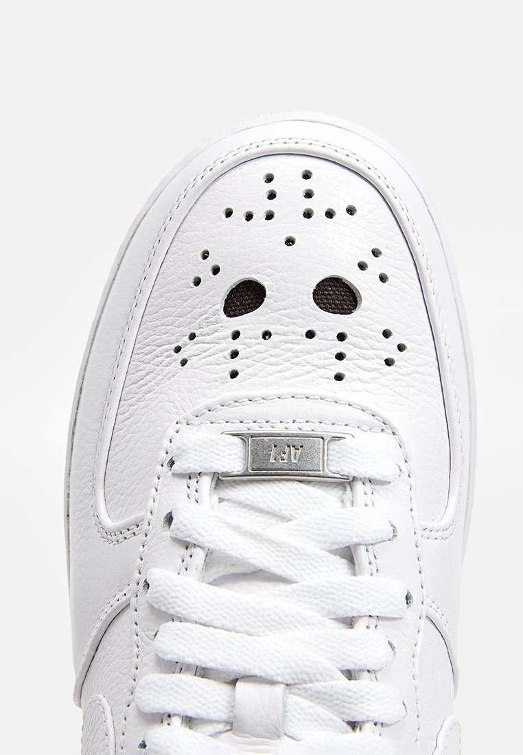 Zapatilla blanca de cuero con cierre de cordones, detalles perforados en la puntera y acentos metálicos plateados. Textura suave con forma de puntera redonda.
