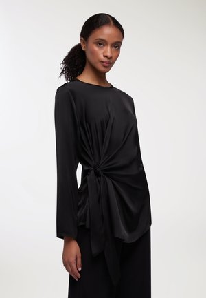 Top in satin nero con maniche lunghe, caratterizzato da un dettaglio frontale attorcigliato legato in vita, texture liscia e scollatura rotonda.
