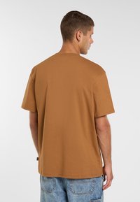 Brun kortærmet T-shirt med en afslappet pasform, lavet af blød bomuld. Har en rund halsudskæring og standard kant, parret med blå jeans.