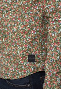 Groene bloemenoverhemd met rode en blauwe patronen; zacht materiaal; heeft een hanglabel met het "ONLY & SONS" logo aan de onderkant.