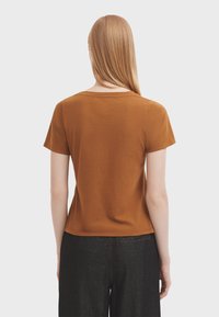 Rustfarvet bomulds T-shirt med korte ærmer, rund halsudskæring og en let løs pasform, parret med mørke denim bukser.
