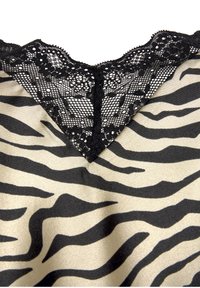 Dierenprinthemdje met een zwarte kanten V-hals. De stof heeft een glanzende beige achtergrond met zwarte zebra-strepen.