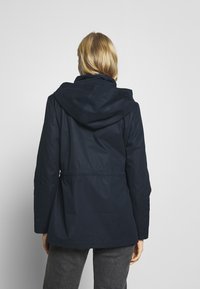 Giacca blu navy con cappuccio e vita stretta, realizzata in tessuto morbido e con maniche lunghe, mostrata dal retro.