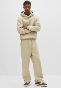 Beige hoodie en bijpassende sweatpants van zachte stof. De hoodie heeft een trekkoord en geribbelde manchetten, terwijl de broek zijzakken heeft.
