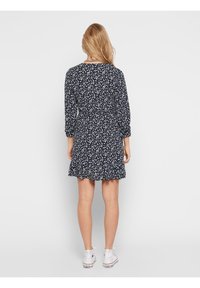 Marineblaues Kleid mit weißem Blumenmuster, Dreiviertelärmel und ausgestelltem Saum. Aus weichem Stoff mit lockerer Passform gefertigt.