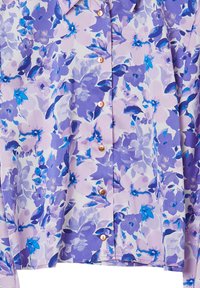 Blouse florale avec des motifs violets et bleus sur un fond clair, dotée d'un col et de boutons couleur cuivre sur le devant.