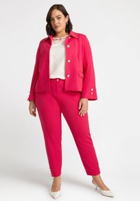 Fuksjowa marynarka dopasowana z metalowymi guzikami, zestawiona z pasującymi spodniami. Strój uzupełnia teksturowana biała bluzka pod spód.