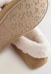 Brown suede slippers with a soft, white faux fur lining. The tan sole features embossed stars and moons. Tag visible on the side.