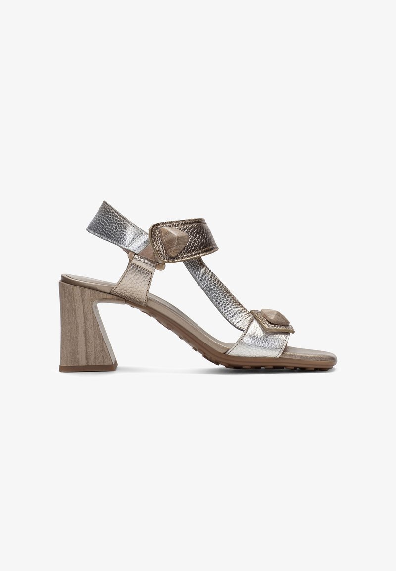 Sandalias de tacón plateadas metálicas con correas texturizadas, que cuentan con una hebilla ajustable y un tacón en forma de bloque similar a la madera. Detalles texturizados en las correas.