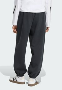 Pantalons de survêtement gris foncé avec des poignets élastiques, fabriqués en tissu doux, associés à des baskets blanches avec des accents noirs.