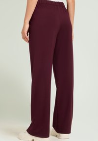 Pantalones anchos en color burdeos con cintura elástica, fabricados en un tejido suave y elástico. Textura lisa sin patrones o detalles visibles.