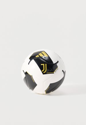 Balón de fútbol blanco y negro con el logo dorado de la Juventus y las rayas de Adidas sobre un fondo claro y liso.
