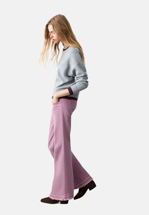 Suéter gris con acentos burdeos, combinado con pantalones rosa acampanados. El conjunto presenta un ajuste relajado y material texturizado. Zapatos marrones completan el look.