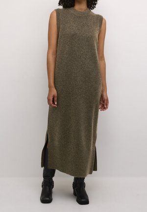 Femme portant une robe midi en maille sans manches vert olive avec des fentes latérales et des bottines noires sur fond uni.
