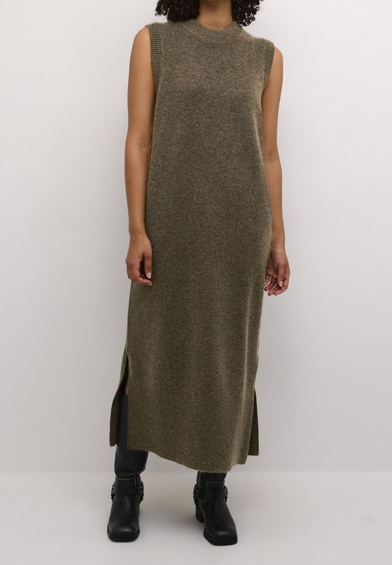 Femme portant une robe midi en maille sans manches vert olive avec des fentes latérales et des bottines noires sur fond uni.