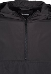 Veste noire à capuche avec une fermeture éclair frontale partiellement fermée, étiquette de la marque Urban Classics visible à l'intérieur du col, et cordons sur la capuche.