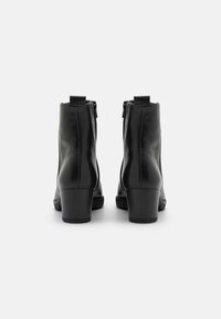 Botas de tobillo de cuero negro con un acabado texturizado, cremalleras laterales y un tacón grueso. El diseño es elegante con un mínimo de accesorios metálicos.