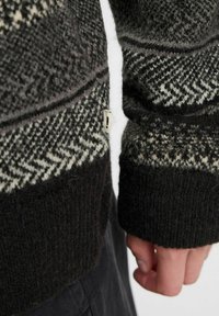 Knitted sweater featuring a dark gray base with light gray and cream geometric patterns. Ribbed cuffs and texture visible on fabric.