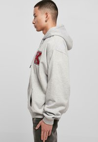 Sweat à capuche gris avec un grand "K" rouge brodé à l'avant, doté d'une capuche avec cordon de serrage, de poches latérales et de poignets côtelés.