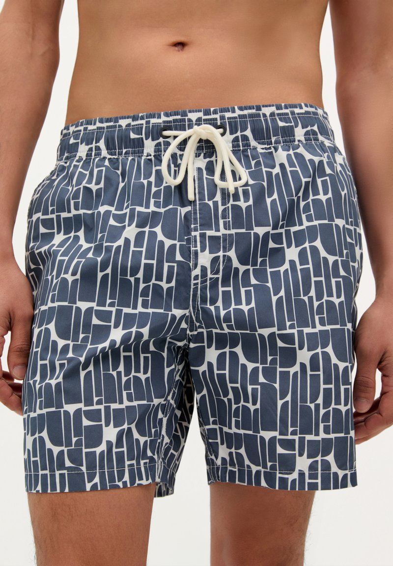Shorts de bain avec un motif géométrique bleu marine et blanc, taille élastique avec cordon de serrage, et un tissu léger et lisse.