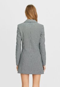 Veste cintrée en motif pied-de-poule noir et blanc, dotée de manches longues, de revers crantés et d'une silhouette ajustée.