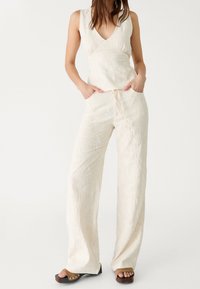 Haut brodé beige clair avec un col en V et un pantalon large assorti. Le tissu présente des motifs floraux et une taille élastique réglable.