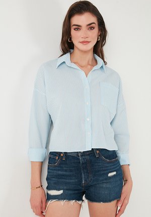 Light blue button-up shirt with thin white stripes, featuring a collar and a chest pocket, paired with dark denim shorts.