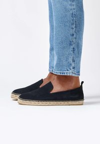 Espadrilles à enfiler en daim bleu marine avec une semelle en corde de jute. Bout arrondi et découpes sur les côtés pour une meilleure aération. Texture lisse et ajustement flexible.
