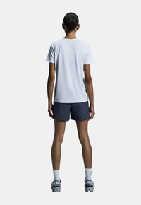 Vit kortärmad skjorta i kombination med marinblå shorts, stående modell från ryggen; har grå sneakers och vita strumpor.