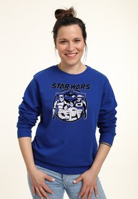 Sudadera azul con un estampado gráfico de personajes de Star Wars en blanco y negro. Puños y dobladillo de canalé, corte relajado.